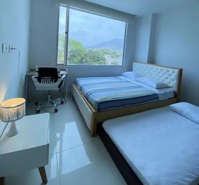 a bedroom with two beds and a desk and a window at Hermoso Apto Familiar en sector Bello Horizonte in Santa Marta