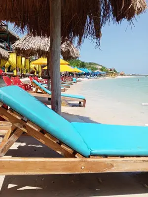 a blue bench on a beach with chairs and umbrellas at casa de vacaciones tierra bomba cartagena de indias in Tierra Bomba
