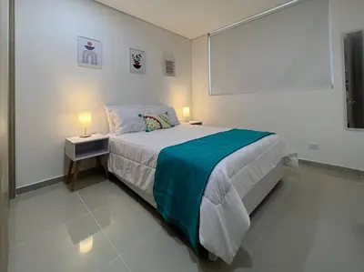 a white bedroom with a bed and two lamps at Moderno y amplio apartamento cerca a la playa! in Cartagena de Indias