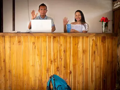 a man and a woman standing behind a wooden counter with a laptop at Mithival Beach Rincón del Mar in Rincón