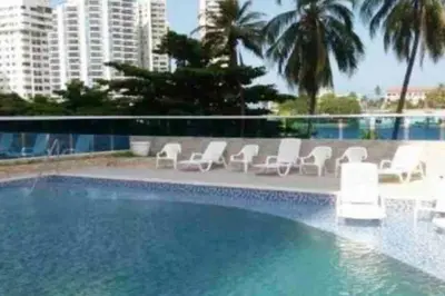 a pool with white chairs and palm trees and buildings at Confort en la zona del Laguito in Cartagena de Indias