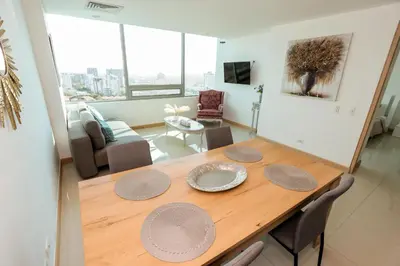 a dining room with a wooden table and a living room at Exclusive Loft Bluegardens Hilton Inn Apartments Barranquilla in Barranquilla