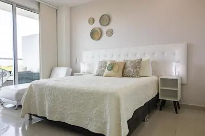 a white bedroom with a large bed and a chair at Apto en Morros Epic Cartagena in Cartagena de Indias