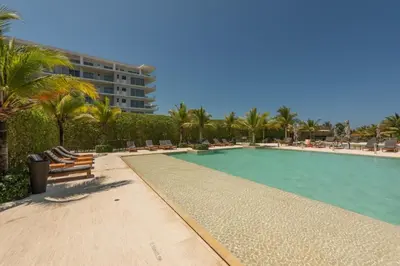 a swimming pool with chairs and palm trees and a building at Frente al Mar, con playa y 4 piscinas en Cartagena in Cartagena de Indias