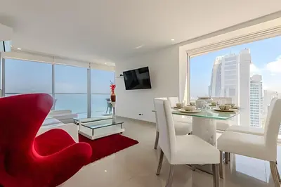 a white dining room with a red chair and a table at Panoramic Sea View & Historic Center “Morros City” in Cartagena de Indias