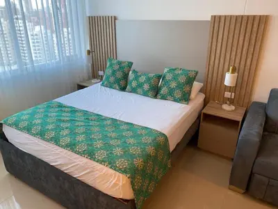 a bedroom with a bed with green sheets and a chair at Apartamento Hotel estelar in Barranquilla