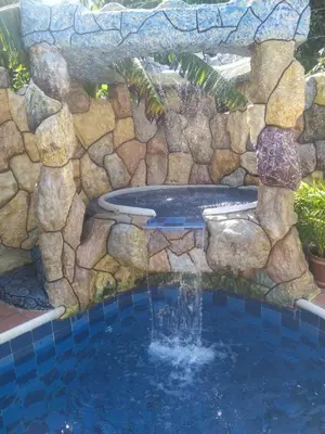 a pool with a stone wall and a fountain at Cabaña La Makuira in Santa Marta