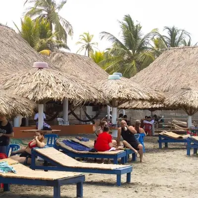 a group of people sitting on the beach under umbrellas at Cabañas Capilla Del Mar in San Bernardo del Viento