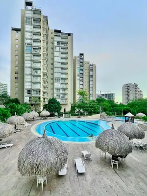 a swimming pool with straw umbrellas and chairs and aominiumominium at Apartamento con vista al mar - Condominio Zazué in Santa Marta