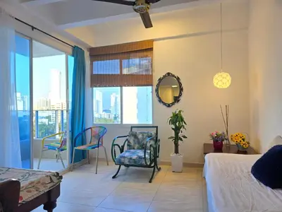 a bedroom with a bed and chairs and a window at Apartamento Caribe Hilton View - Piso 7 in Cartagena de Indias