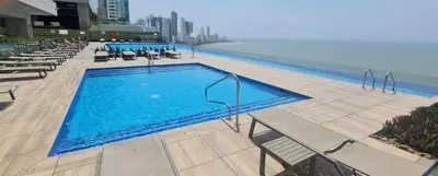 a large swimming pool with chairs and the ocean at luxury apartemt bay front 1bed 2703 in Cartagena de Indias