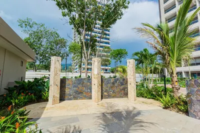 a stone fence in front of a building with palm trees at Apto Lujo Vista Mar Piscina AC WIFI Playa a 3 min en Santa Marina in Santa Marta