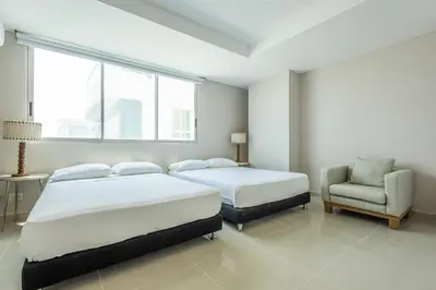 a bedroom with two beds and a chair and a window at Luxurious Beachfront 3BR, Pool & Ocean Views in Cartagena de Indias