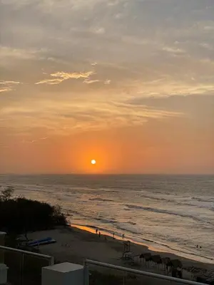 a sunset over the ocean with people on the beach at La Rosita in Puerto Colombia