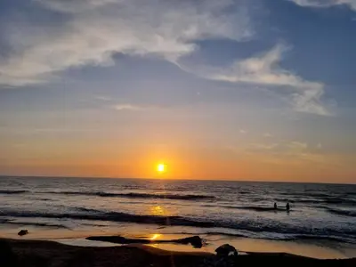 a sunset on the beach with people in the water at HELENA Beach House in La Rada