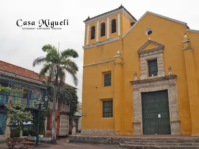 a yellow building with a clock tower next to a palm tree at Casa Migueli, exclusiva casa con jacuzzi en terraza in Cartagena de Indias