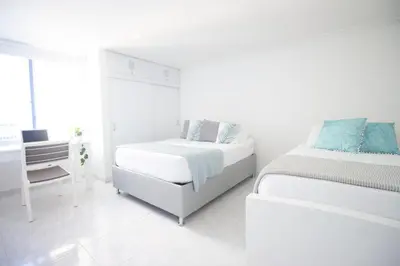 a white bedroom with two beds and a desk at Riviera del Mar - Apartamento con vista panorámica al mar in Cartagena de Indias