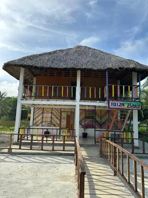 a building with a straw roof and a boardwalk at Ibiza beach in Moñitos