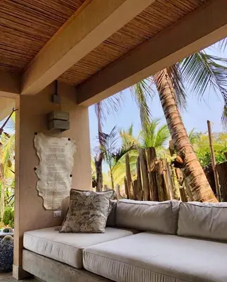 a couch sitting on a porch with palm trees at En La Casa Del Mar in Moñitos