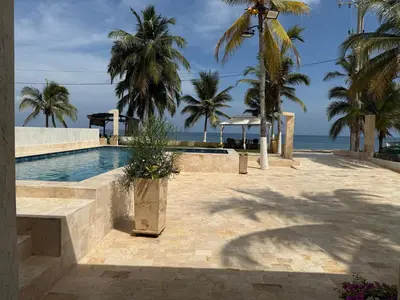 a swimming pool with palm trees and the ocean at Cabaña Aledan in Coveñas