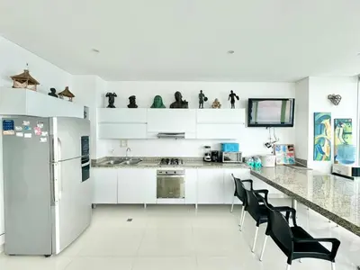 a white kitchen with black chairs and a refrigerator at Apartamento de lujo frente al mar in Coveñas