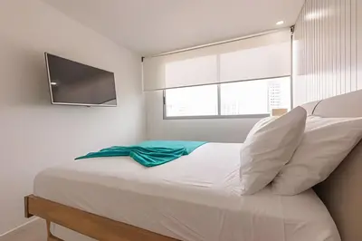 a bedroom with a bed with white sheets and a television at Lujoso Apto de 2 habitaciones en piso 15 in Cartagena de Indias