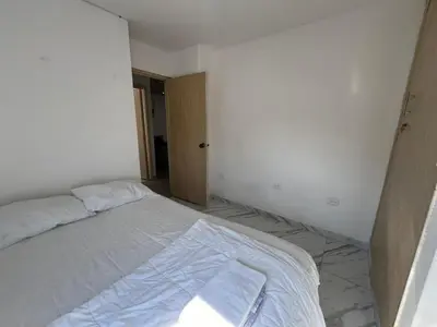 an unmade bed in a white room with a door at Luz in Barranquilla