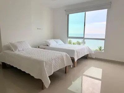 two beds in a white room with a large window at Hermoso Apartamento Frente al Mar 3 Habitaciones AR54 in Coveñas