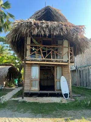 a surfboard is sitting outside of a thatched building at CARPE DIEM oceanfront cabin private beach in San Bernardo del Viento