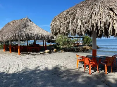 a beach with two chairs and a table and a straw umbrella at Habitacion Ely Johana in Coveñas