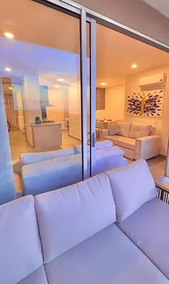 a living room with white furniture and a large glass window at Aqua Marine Suite - Santa Marina Condo in Santa Marta