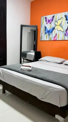 a bedroom with a bed with an orange wall and a mirror at hotel hispanoamericano in Barranquilla