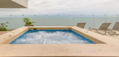 a swimming pool with chairs and the ocean in the background at Luxury Oceanfront Apartment Spiaggia 2BR 3BA Playa azul Cartagena in Cartagena de Indias
