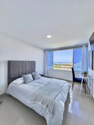 a white bedroom with a large bed and a chair at Apartamento con vista al mar - Riviera Mulata Beach in Cartagena de Indias