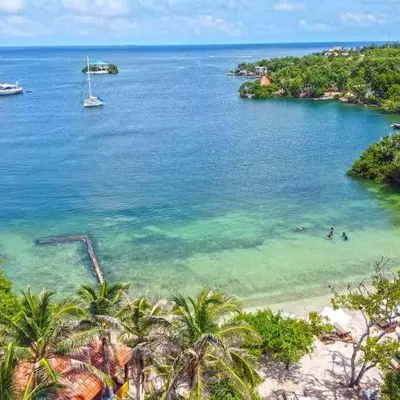 a beach with palm trees and a sailboat in the water at Eco Hotel Islabela Deluxe in Isla Grande