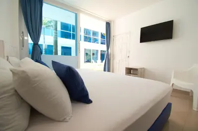 a bedroom with a white bed with blue pillows and a window at Palma Linda Coveñas by Bernalo Hotels in Coveñas