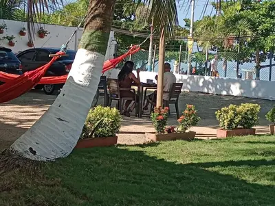 two people sitting at a table under a palm tree at Ortimar in Tolú