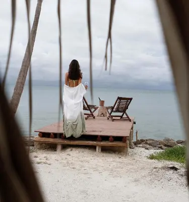 a woman sitting on a bench on the beach at Cabana SalSiPuedes in Tintipan Island