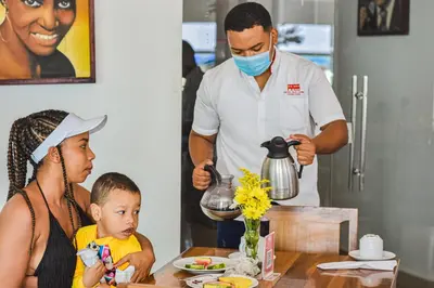 a woman and a child and a man in a mask preparing food at Hotel Isla Capri in Cartagena de Indias