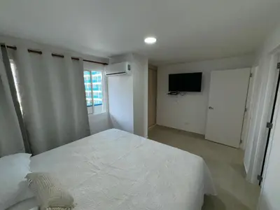 a white bedroom with a bed and a television at Apartamento Vista Lateral a la Playa By ICDI in Cartagena de Indias