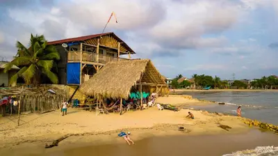 a building on a beach with people on the sand at Hostel Blue Sea Rincon del Mar in Rincón