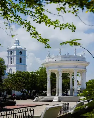 a white building with a clock tower in the background at Hotel Diamante Real Cienaga in Ciénaga