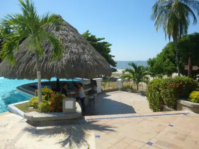 two people sitting under a straw umbrella next to a pool at Costa Azul Suites 906 in Santa Marta