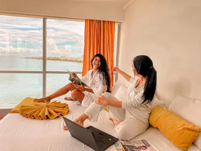 two women sitting on a bed with a window at Hotel Costa del Sol in Cartagena de Indias