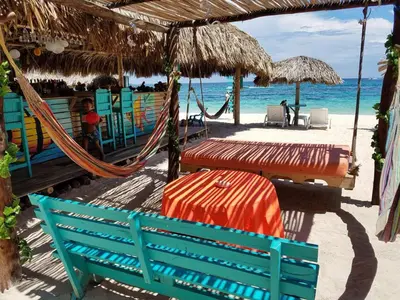 a hammock and chairs on a beach with the ocean at The Wizard & Bar BARU in Playa Blanca