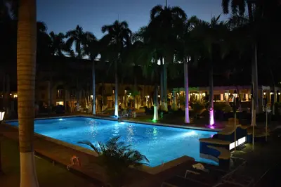 a swimming pool at night with palm trees and lights at Hotel El Prado in Barranquilla