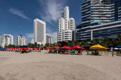 a beach with red and yellow umbrellas and buildings at Hotel Regatta Cartagena in Cartagena de Indias