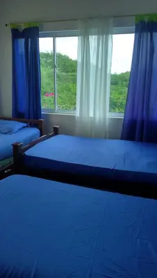 a bedroom with two beds and a window with blue curtains at Casa de Campo Palmarito in Tubará