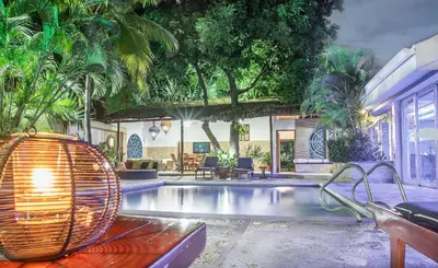 a swimming pool with benches and trees and a house at Hotel Santorini Express y Cabañas in Santa Marta