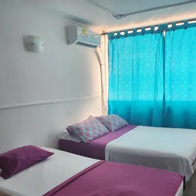 two beds in a room with blue curtains and purple pillows at Arriendos Yeny in Cartagena de Indias